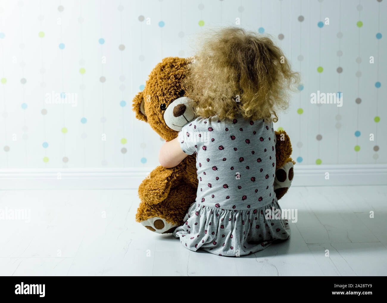 Little curly haired girl crying in her room. Little girl misses it`s mom. Stock Photo
